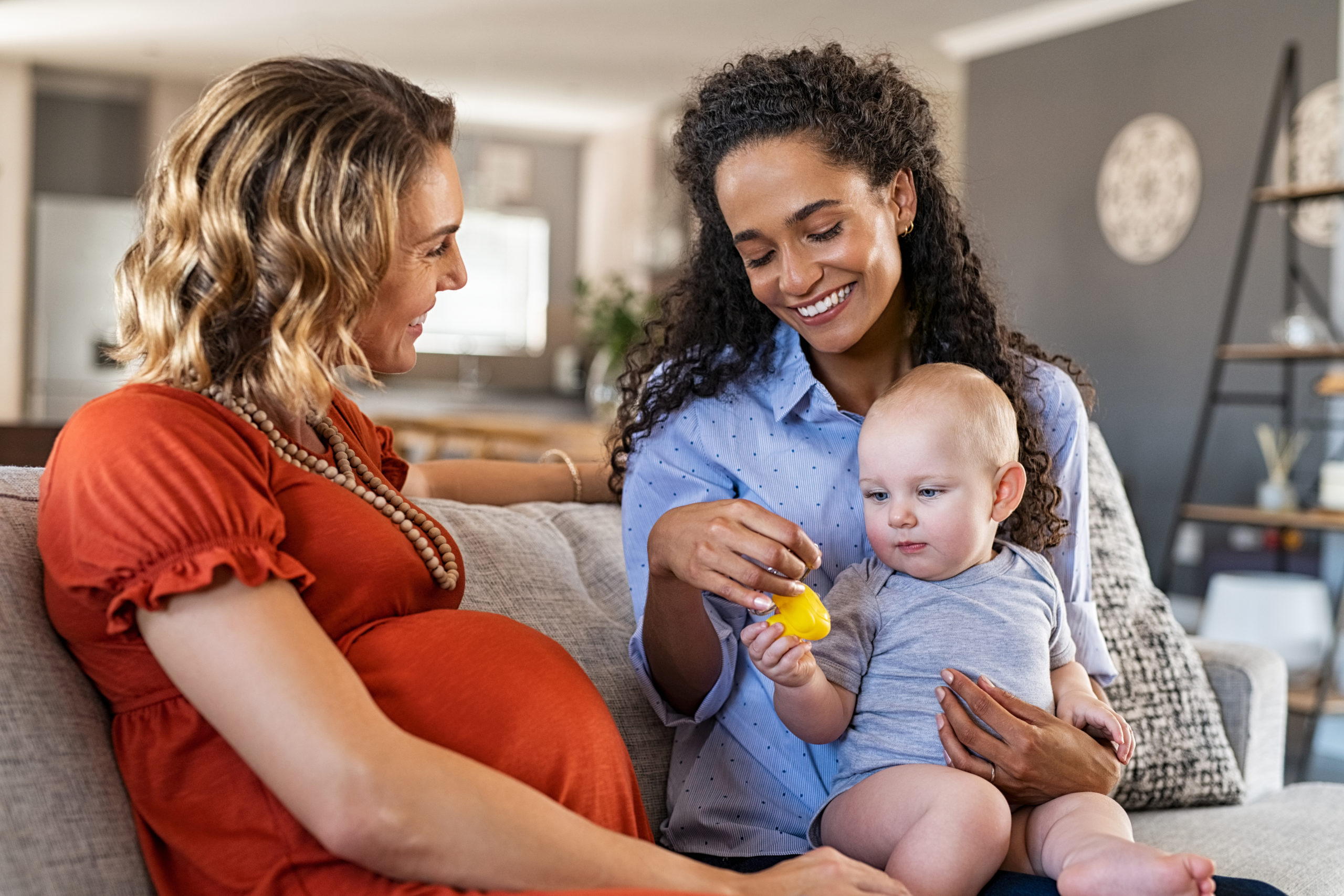 Happy multiethnic friends with child sitting on couch. Pregnant
